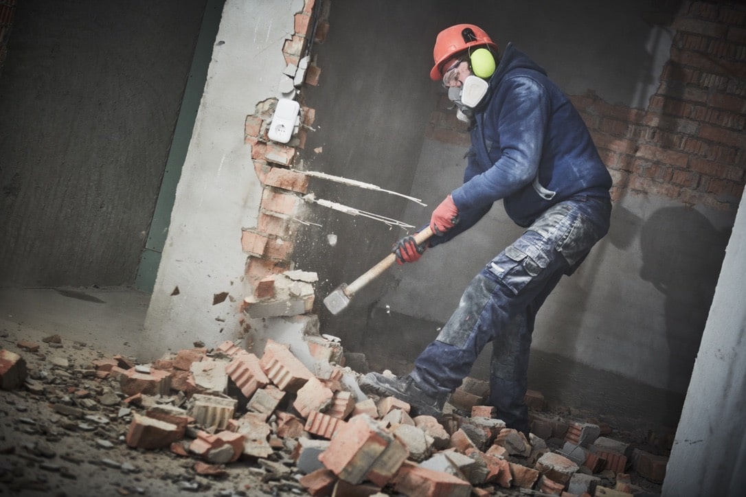 man demolishing brick from wall construction site
